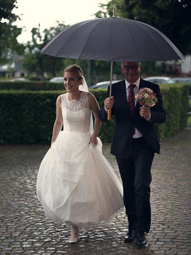 Braut und Brautvater mit Regenschirm auf dem Weg zur Kirche